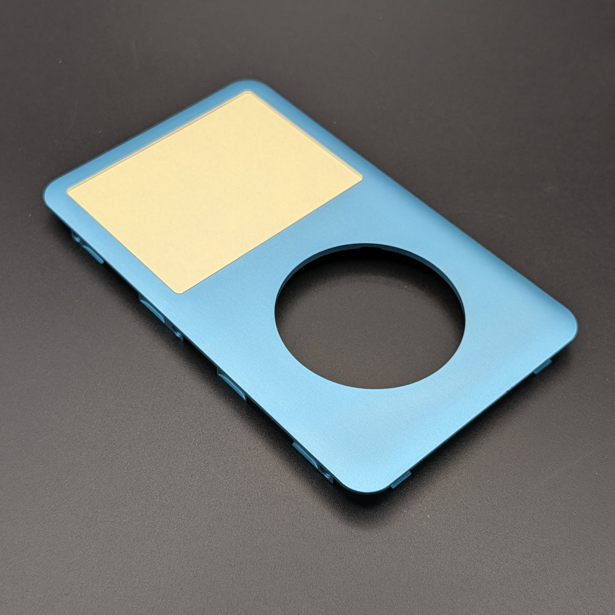 A light blue aluminum replacement case for an iPod Classic, featuring a circular cutout, shown on a dark gray background.