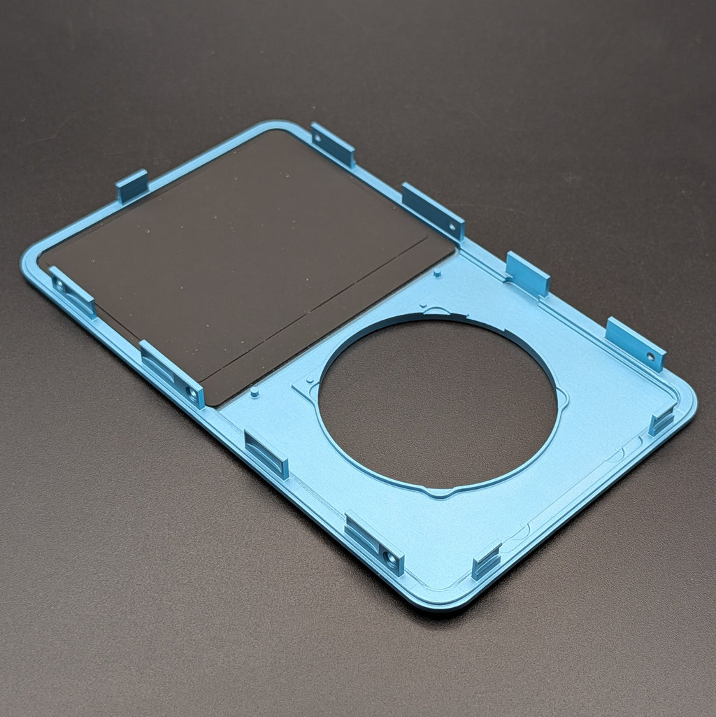 A light blue replacement frame with a circular cutout and mounting slots, shown on a dark gray background.