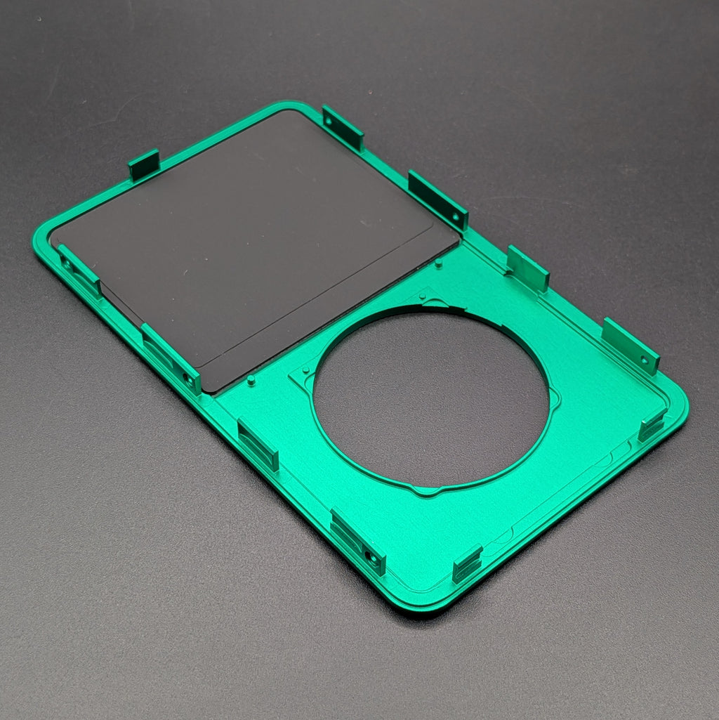 A green plastic replacement frame or cover with a circular cutout and mounting tabs, shown on a dark gray textured background.