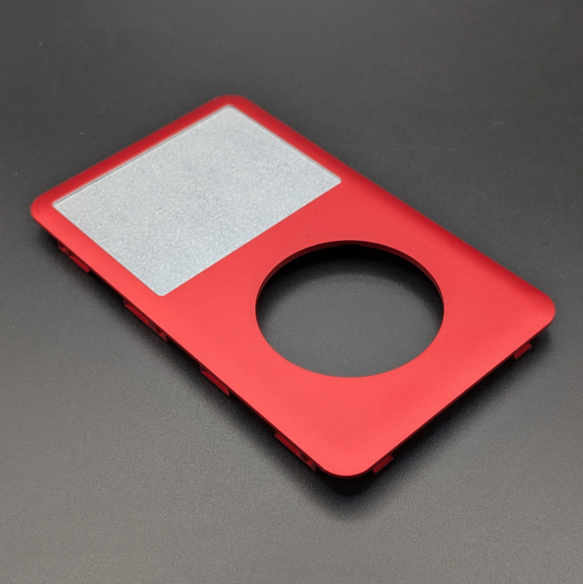A red metal replacement shell designed for an iPod Classic, featuring a screen insert and a circular cutout, shown on a dark gray background.