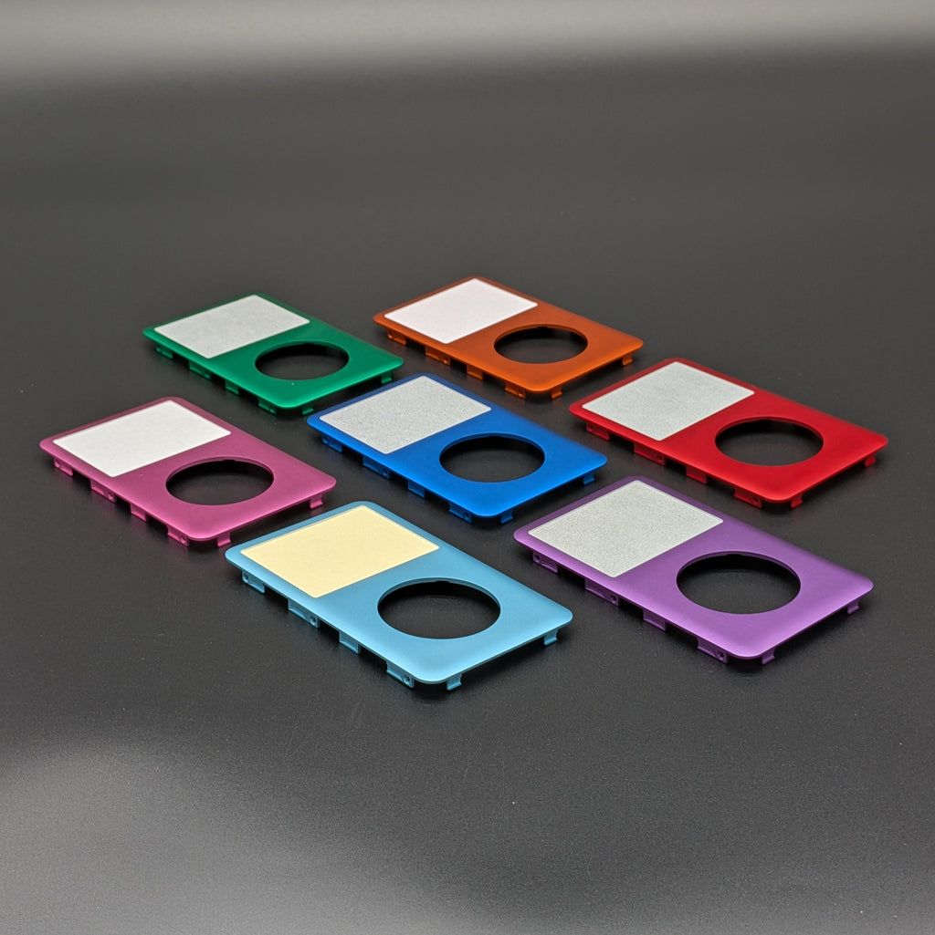 Six colorful rectangular metal components with circular cutouts and silver screens, shown in green, orange, red, pink, blue, and purple on a dark gray background.
