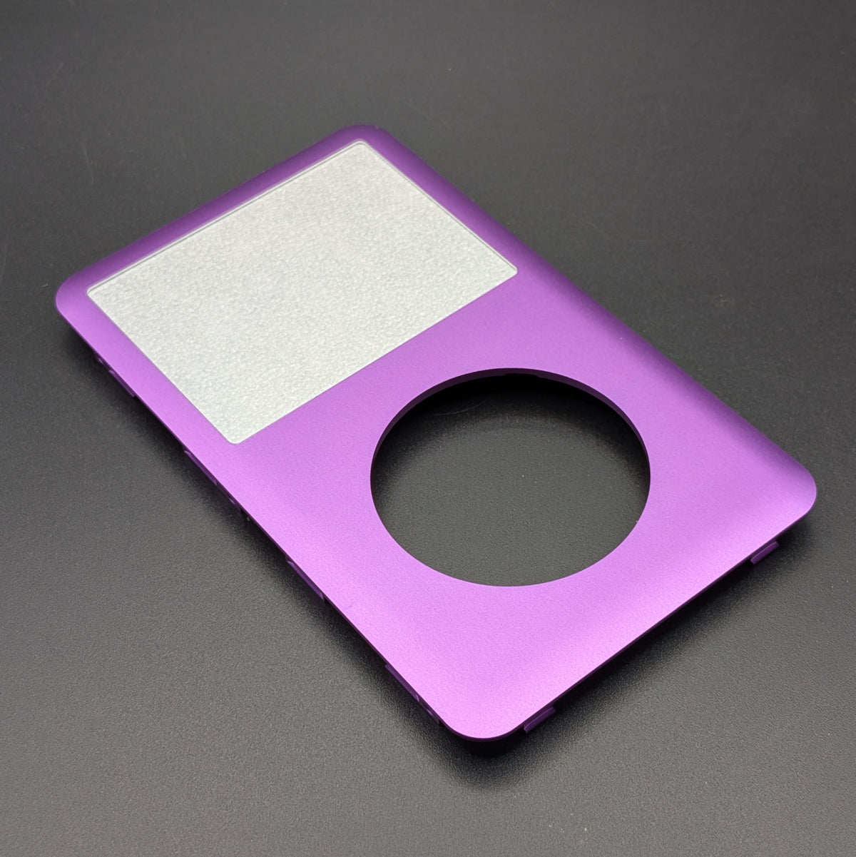 A purple metallic replacement faceplate or backplate for an iPod Classic, featuring a cutout for the circular touchpad and a textured silver panel, shown on a dark gray background.