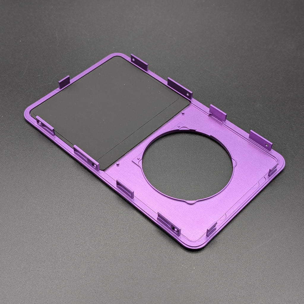 A purple plastic replacement frame or bezel component with a circular cutout and mounting tabs, shown on a dark gray textured background.