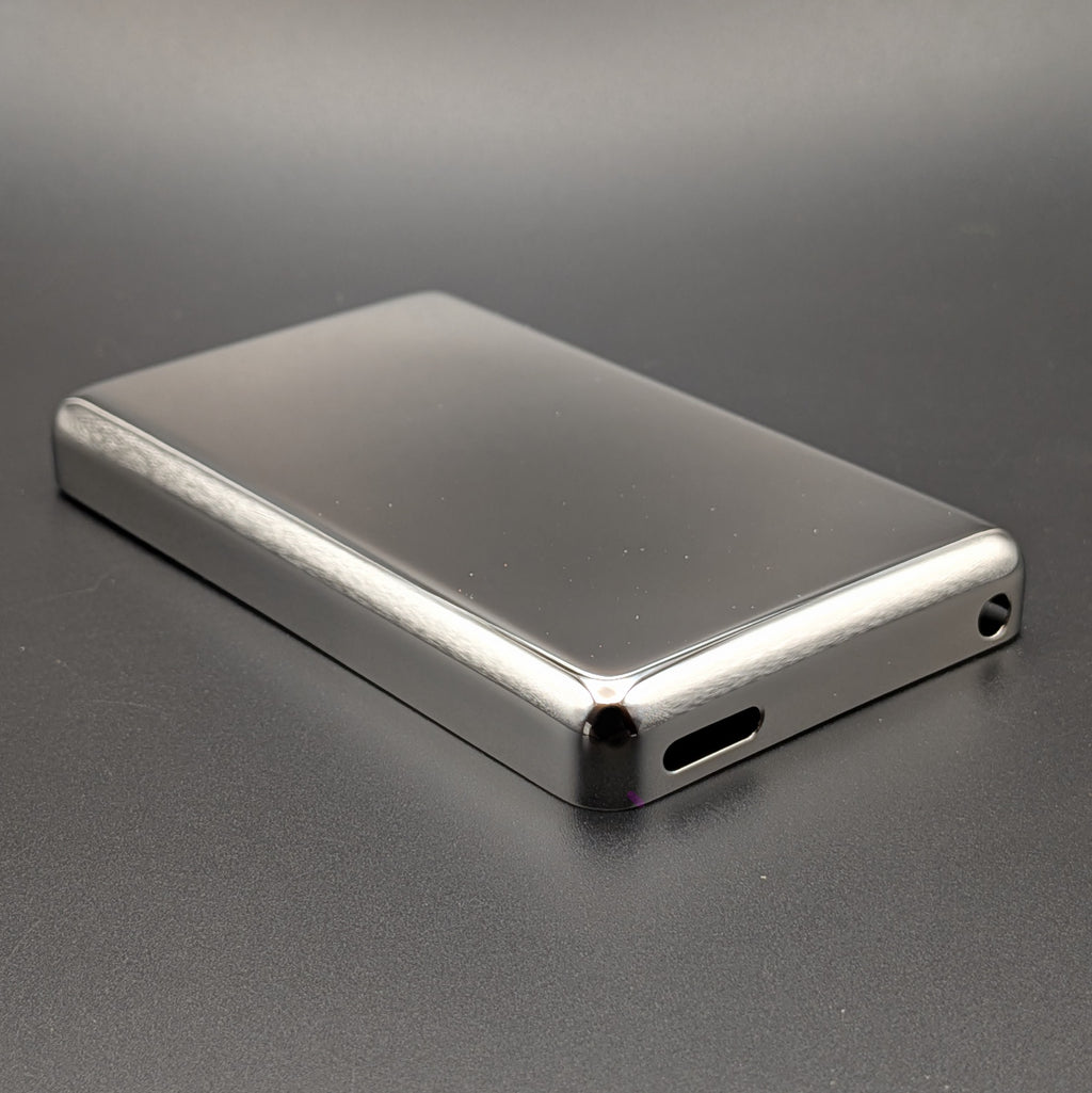 A rectangular metallic silver iPod back plate, shown at an angle on a dark gray textured surface.