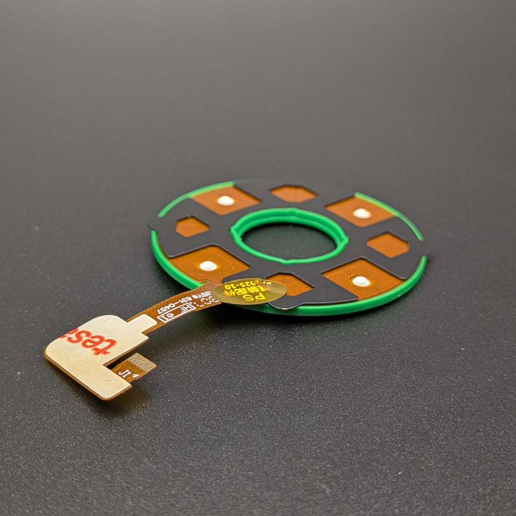 Reverse side of a replacement electronic control module with a flexible flex cable, photographed on a dark gray textured surface.