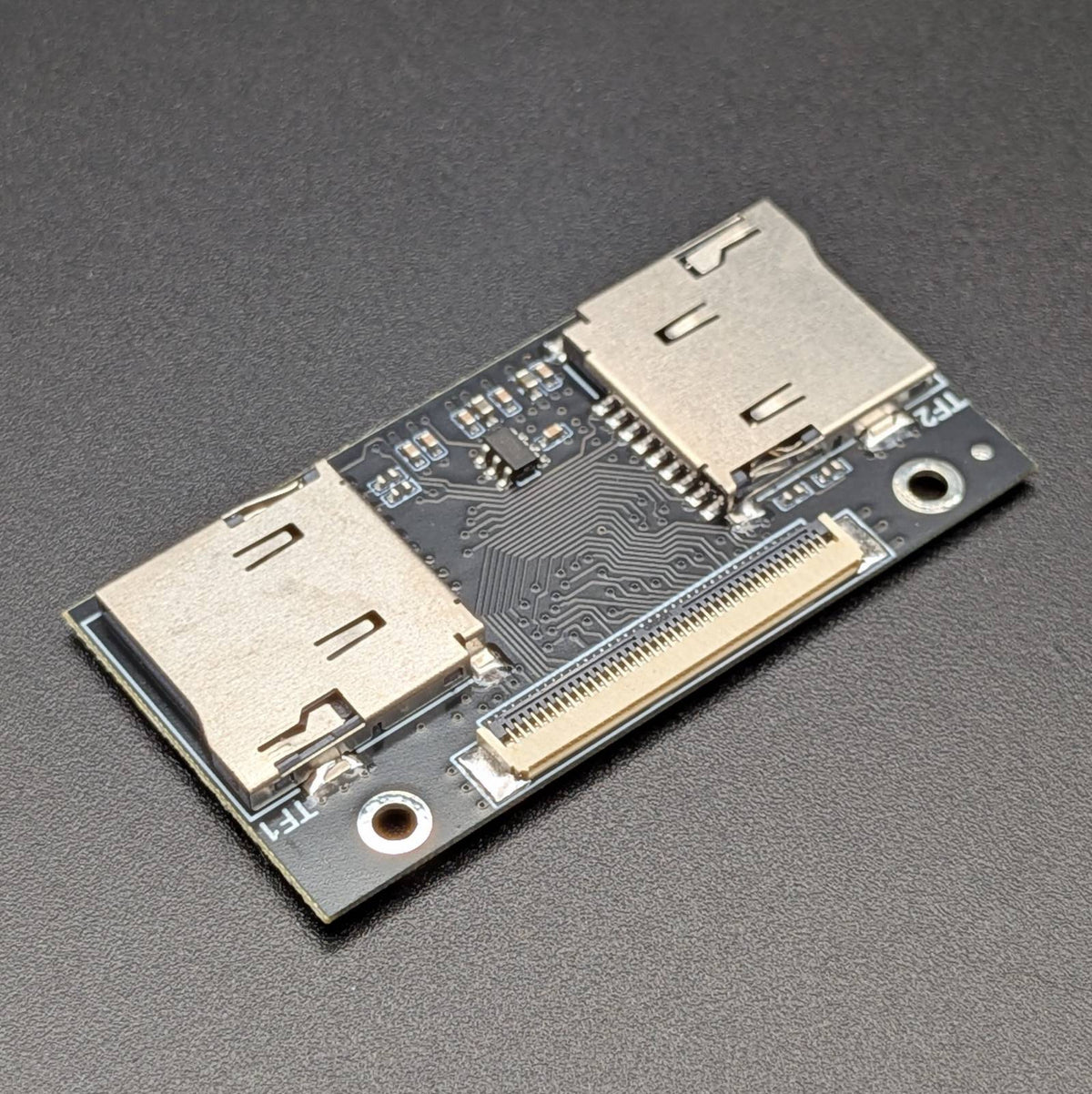 A compact electronic adapter board featuring two silver metal Micro SD ports and a gold-plated PCIe connector, mounted on a dark PCB over a textured dark gray background.