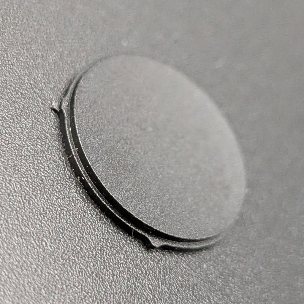 A close-up of a small circular black button resting on a textured dark gray surface.