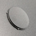 A close-up of a small circular black button resting on a textured dark gray surface.