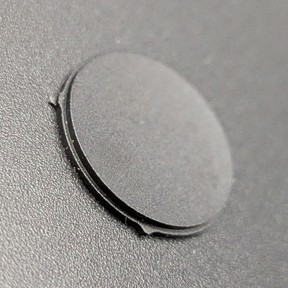 A close-up of a small circular black button resting on a textured dark gray surface.