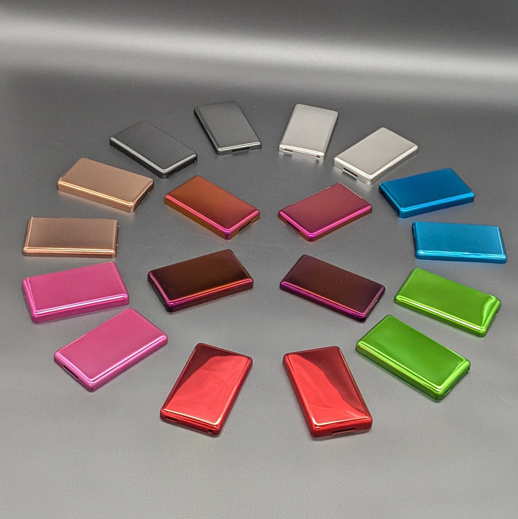A collection of small rectangular metallic ipod Back plates arranged in a circle on a gray surface, showing multiple color options including silver, white, rose gold, copper, orange, pink, red, green, and blue.
