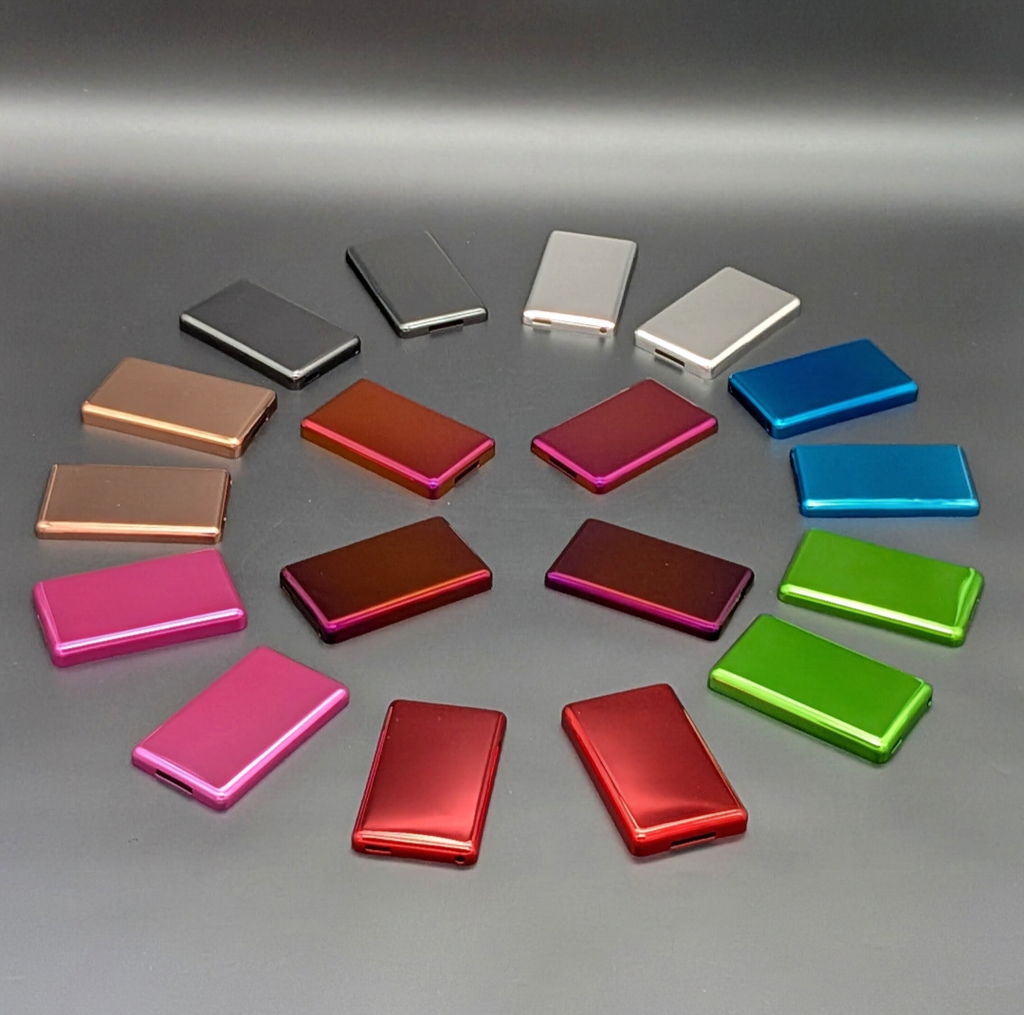 A collection of iPod metal back plates arranged in a circle on a gray surface, showing multiple color options including silver, white, bronze, orange, magenta, blue, green, and pink.