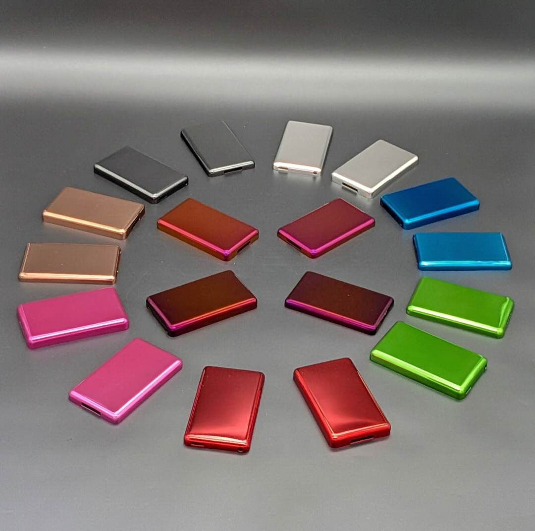A collection of iPod metal back plates arranged in a circle on a gray surface, showing multiple color options including silver, white, bronze, orange, magenta, blue, green, and pink.