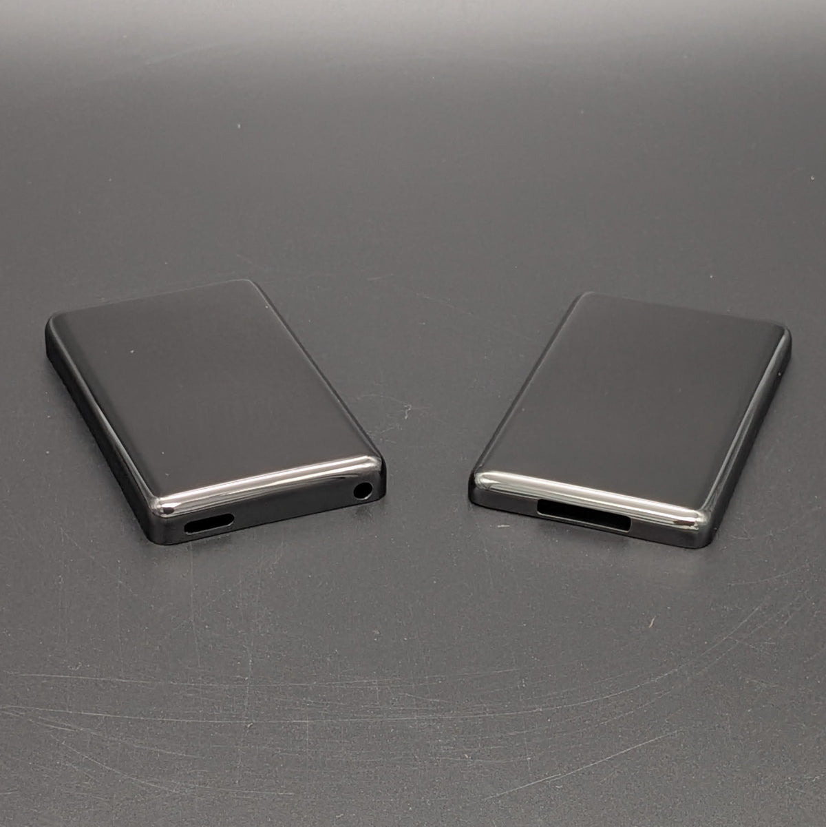 Black rectangular iPod back plates, shown from the back on a dark gray textured surface.