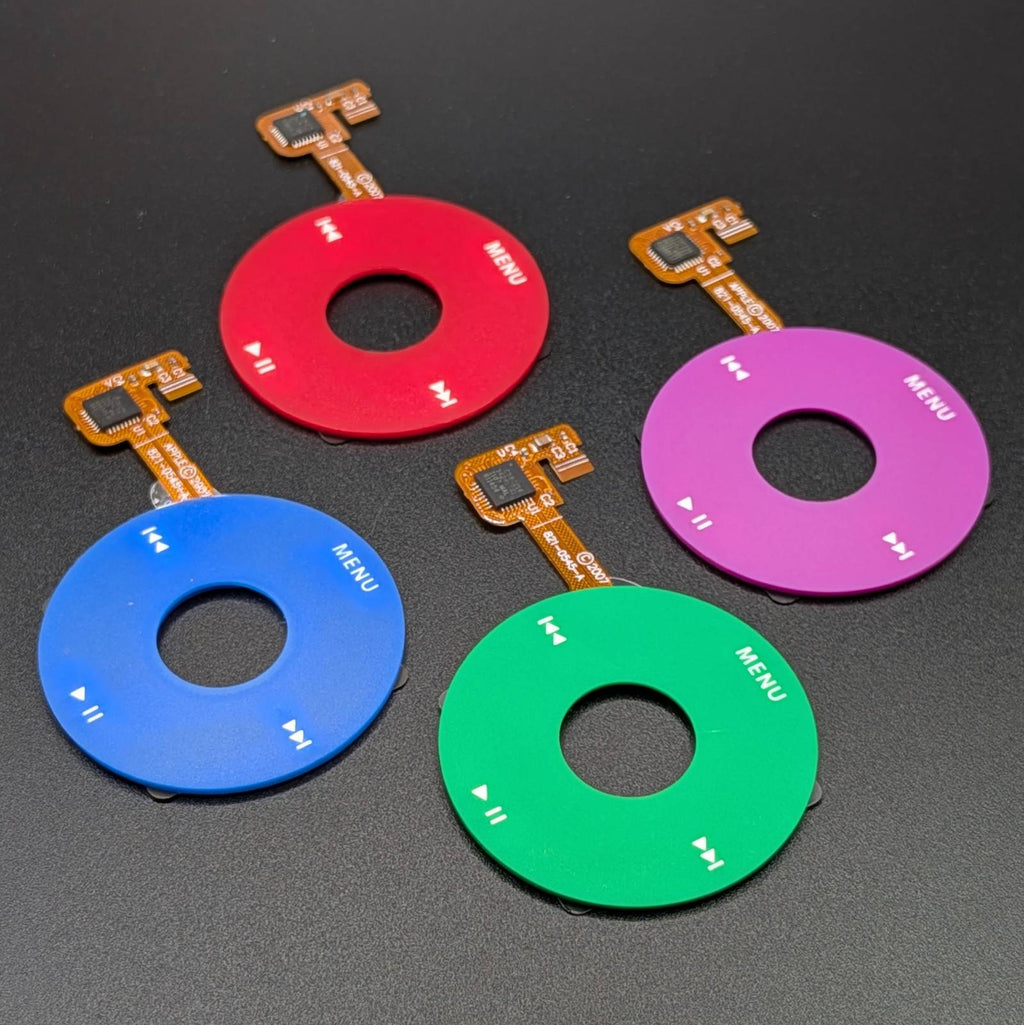 Four circular electronic control modules in red, blue, green, and purple, arranged on a dark textured background. Each module features a central cutout, white printed control icons, and a small orange flex cable connector.